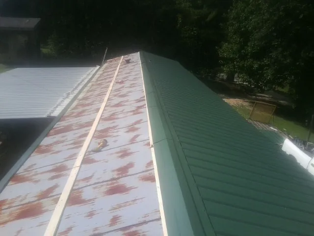 Old rusted panels beside newly installed green metal roofing — Wind Damage Roof Repair by Roofing Brothers in Banner Elk
