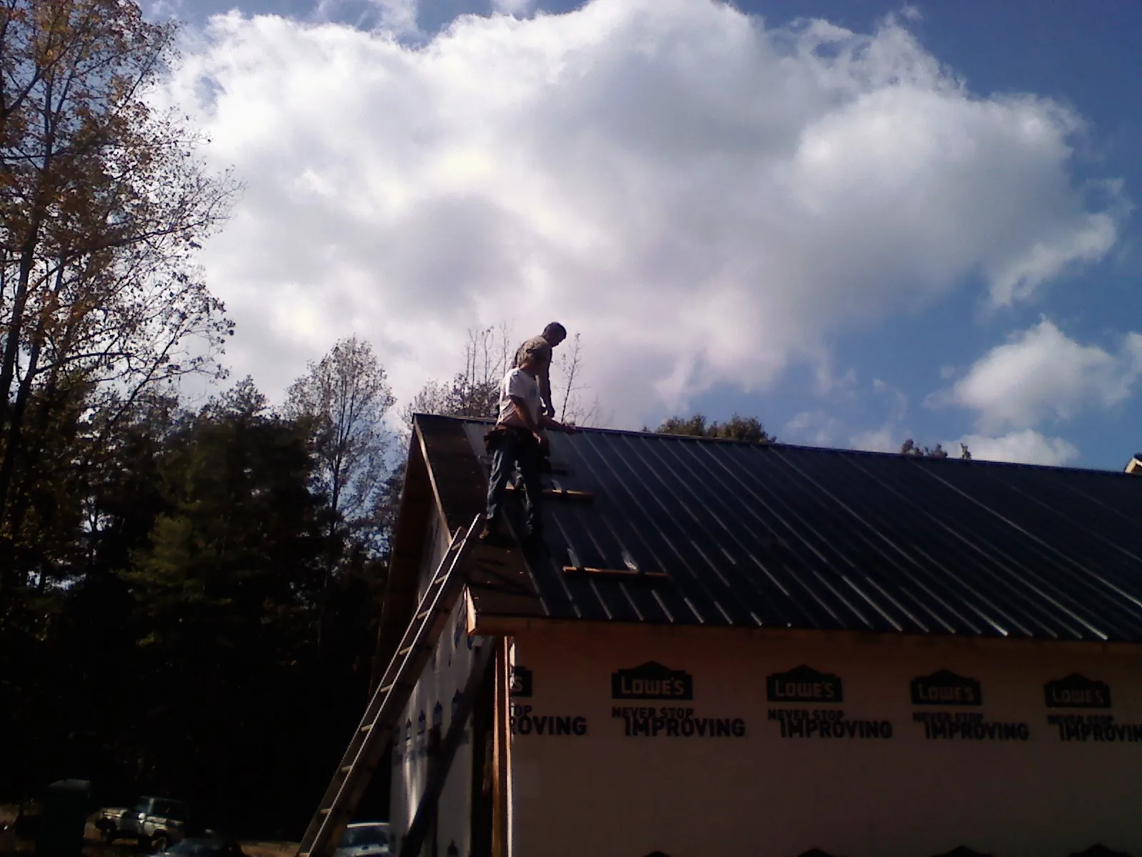 Roofer fastening dark metal panels high against a cloudy sky, from a Roof Inspection job in Banner Elk