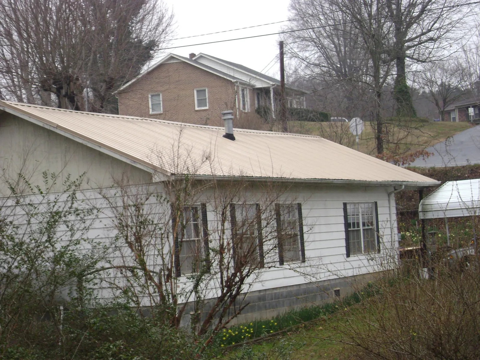 Tan metal roof on a white sided house set into a hillside — Commercial Roofing by Roofing Brothers in Banner Elk