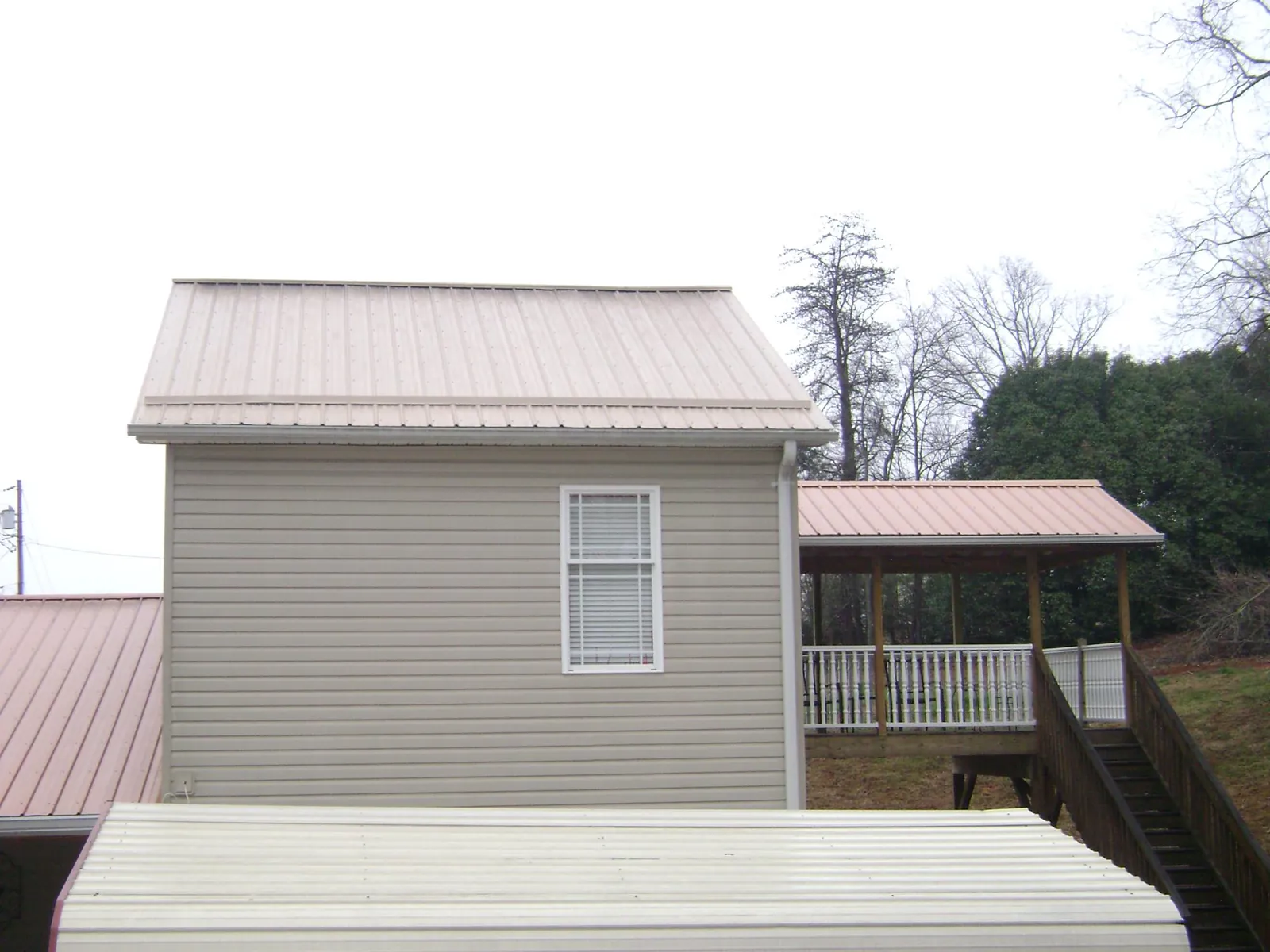 Tan metal roofs on a two story addition and attached porch, from a Roof Replacement job in Banner Elk